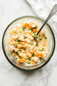This image shows a top-down view of a mixing bowl containing the fully combined mini chicken pot pie filling, a creamy mixture of shredded chicken, vegetables, and cream of chicken soup.
