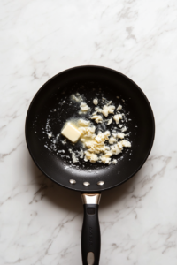 This image shows minced garlic sizzling in melted butter in a pan, releasing a rich and aromatic fragrance.