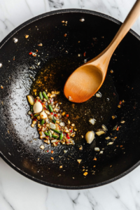 A close-up image of a pan with hot oil, garlic, and ginger being sautéed to release their aroma.