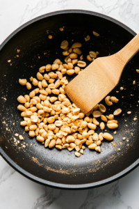 This image shows raw peanuts being roasted in a pan until golden brown and fragrant, adding a rich nuttiness to the Kung Pao Chicken.