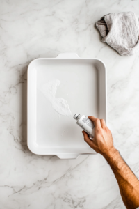 This image shows a baking pan being greased and prepared for assembling the meatloaf casserole, ensuring easy removal after baking.