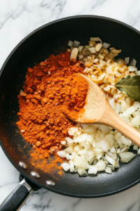 This image shows minced garlic and a blend of fragrant spices being added to the sautéed onions, releasing their deep, warm flavors.
