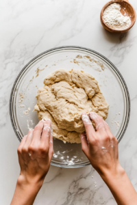This image shows hands kneading dumpling dough on a lightly floured countertop to achieve the perfect consistency.