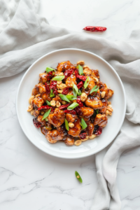 This image shows a beautifully plated serving of Kung Pao Chicken, glistening with sauce and topped with crispy peanuts and fresh scallions for a restaurant-quality finish.