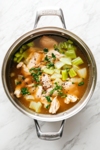 This image shows a fully cooked chicken being lifted out of the stockpot after simmering, ready to be shredded. Step 6: Straining Vegetables