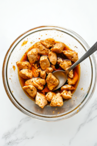 This image shows bite-sized chicken pieces being coated in a rich, savory marinade to enhance the depth of flavor before cooking.