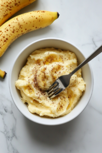 This image shows ripe bananas being mashed in a bowl with a fork, creating a smooth and creamy texture for the cookie batter.