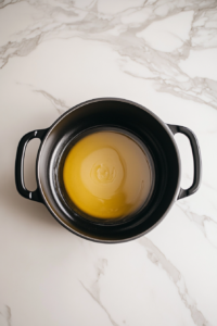 This image shows a large pot on the stovetop with a golden mixture of melted butter and olive oil, heated and ready for browning the chicken for a delicious homemade stew.
