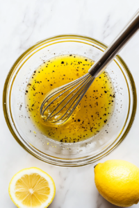 This image shows a small bowl of homemade dressing being whisked together, combining olive oil, lemon juice, and seasonings to enhance the flavors of the tomato cucumber feta salad.