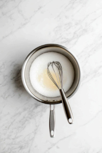 This image shows a saucepan filled with sugar, corn syrup, and water being stirred together, forming the base for the sweet and crunchy candy apple coating.