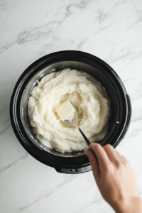 This image shows a spoon mixing butter, cream, and seasonings into mashed potatoes, ensuring a smooth and uniform texture.