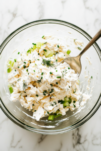 This image shows mayonnaise, sour cream, celery, dill, and chives being mixed into the shredded whitefish for a creamy consistency.