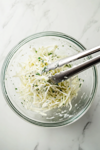This image shows fresh shredded cabbage and carrots being tossed with a creamy dressing, ensuring an even, well-coated coleslaw mix.