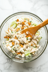 This image shows all the ingredients being tossed together in a bowl, ensuring the chicken, almonds, and celery are evenly coated with the creamy dressing.