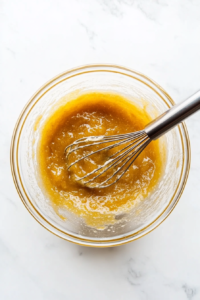 This image shows a bowl with flour, eggs, and seasonings being whisked together to form a smooth batter, ready to coat the chicken pieces.