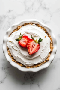 This image shows a half-cut strawberry delicately placed on top of the whipped cream, adding a decorative and flavorful finishing touch.