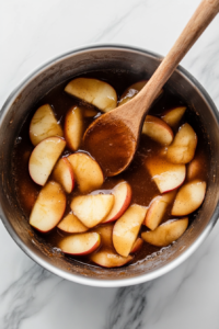 A rich brown sugar mixture being poured over warm, tender apple slices, coating them in a sweet, cinnamon-spiced glaze for a perfect homemade pie filling.