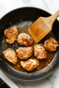 This image shows a hand pouring chicken broth into the skillet, helping to deglaze the pan and create a flavorful garlic butter sauce.