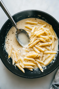 This image shows pasta water being poured into the skillet, helping to adjust the consistency of the creamy sauce for a smooth and velvety texture.