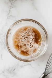 This image shows the activated yeast mixture being poured into the bowl of wet ingredients, beginning the process of making the dough for Polish cheese babka.