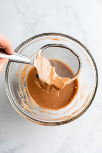 This image shows a thickened glaze being strained through a fine-mesh sieve to remove any lumps, ensuring a smooth texture.