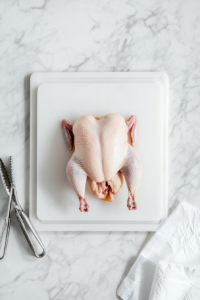 This image shows a whole raw chicken being cleaned, with the neck and innards removed in preparation for making Chicken and Dumplings.