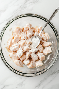 This image shows raw chicken pieces being coated in a light batter, ensuring a crispy texture when fried.