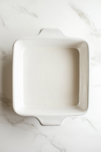 This image shows a baking dish being greased and lined with parchment paper to prevent sticking, ensuring easy removal of the baked pumpkin bars.