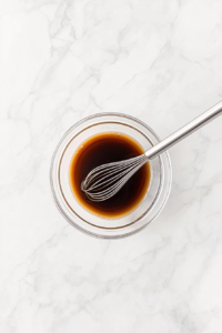 This image shows a glossy, deep-colored sauce being mixed in a bowl, combining soy sauce, vinegar, sugar, and cornstarch for the perfect Kung Pao glaze.
