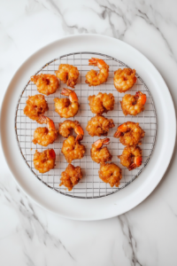 This image shows freshly fried shrimp being transferred to a paper towel-lined plate, ensuring they stay crispy while absorbing any extra oil.