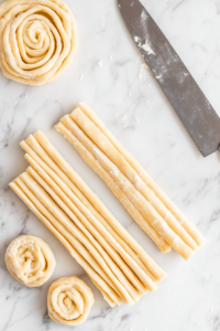 This image shows dough being carefully rolled into a log and sliced into evenly sized rolls, ready for baking.