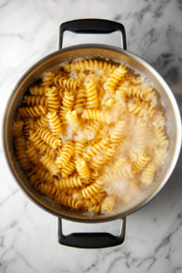 This image shows a pot of rotini pasta cooking in boiling water, preparing the perfect base for a creamy chicken bacon ranch pasta dish.