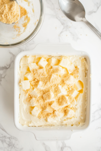 This image shows cubed cream cheese being scattered across the cake mix layer, adding a creamy and rich texture to the dump cake.