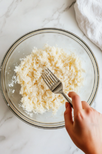 This image shows the flaked whitefish being further shredded into finer pieces for a smooth and even salad texture.