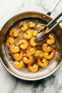 This image shows freshly fried shrimp being transferred to a paper towel-lined plate, ensuring they stay crispy while absorbing any extra oil.