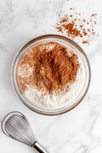 This image shows flour, cinnamon, and other dry ingredients being sifted together to create a light, airy cake batter.