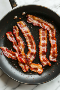 This image shows strips of bacon sizzling in a skillet, turning golden and crispy, ready to add a smoky crunch to the pasta dish.