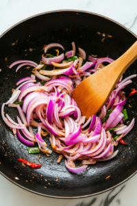 This image shows thinly sliced onions being sautéed until golden and fragrant in a pan.