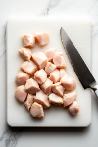 This image shows raw chicken breast being sliced into bite-sized pieces on a cutting board, preparing for cooking in the Broccoli Chicken Penne Pasta recipe.