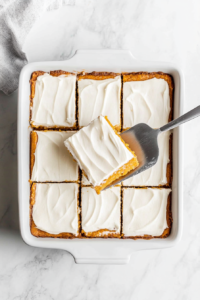 This image shows pumpkin bars being sliced into neat squares and arranged on a serving plate, revealing their soft texture and creamy frosting on top.