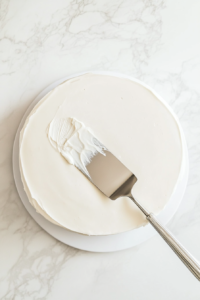 This image shows an offset spatula gently spreading the mirror glaze for an even and polished finish.