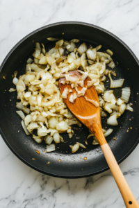 This image shows finely chopped onions being sautéed in a pan, turning golden brown to create a rich and flavorful base for the curry.