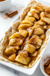 This image shows spoonfuls of warm apple pie filling with a dash of cinnamon being added to the center of the puff pastry, ready to be folded and baked.