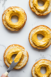 This image shows Dijon mustard being spread evenly on the bagel, adding a tangy and flavorful layer to the turkey sandwich.