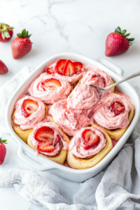 This image shows a spatula spreading rich cream cheese frosting over warm cinnamon rolls, melting slightly for a deliciously gooey topping.
