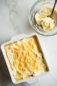 This image shows a spatula spreading lemon pie filling evenly across the bottom of a greased baking dish, creating the first layer of the dump cake.