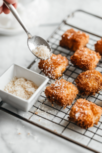 This image shows a hand lightly sprinkling MSG over a batch of crispy fried chicken, enhancing the savory, umami taste.