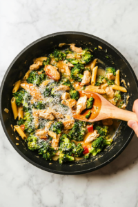 This image shows freshly grated Parmesan cheese being sprinkled over the creamy Broccoli Chicken Penne Pasta, adding a savory and delicious finishing touch.