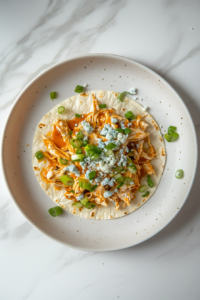 This image shows crumbled blue cheese and freshly chopped scallions being sprinkled on top of Buffalo chicken tacos, adding a tangy and aromatic finishing touch.
