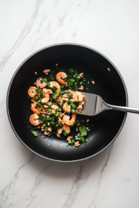 This image shows finely chopped cilantro being sprinkled over sizzling shrimp, adding a burst of fresh, herbaceous flavor to the dish.